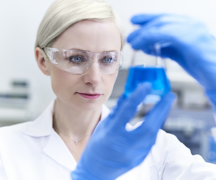A woman in a lab coat holds a beaker containing a vibrant blue liquid, focused on her experiment.